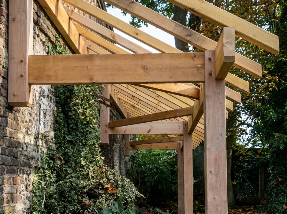 Pergola en bois massif neuf, fixée contre un mur en brique ancienne recouvert de lierre